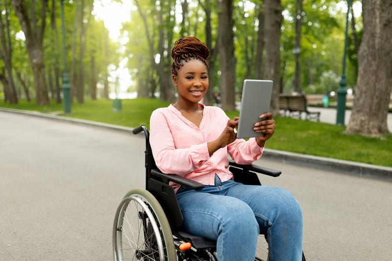 Femme souriante en fauteuil roulant utilisant une tablette, illustrant l'accessibilité numérique