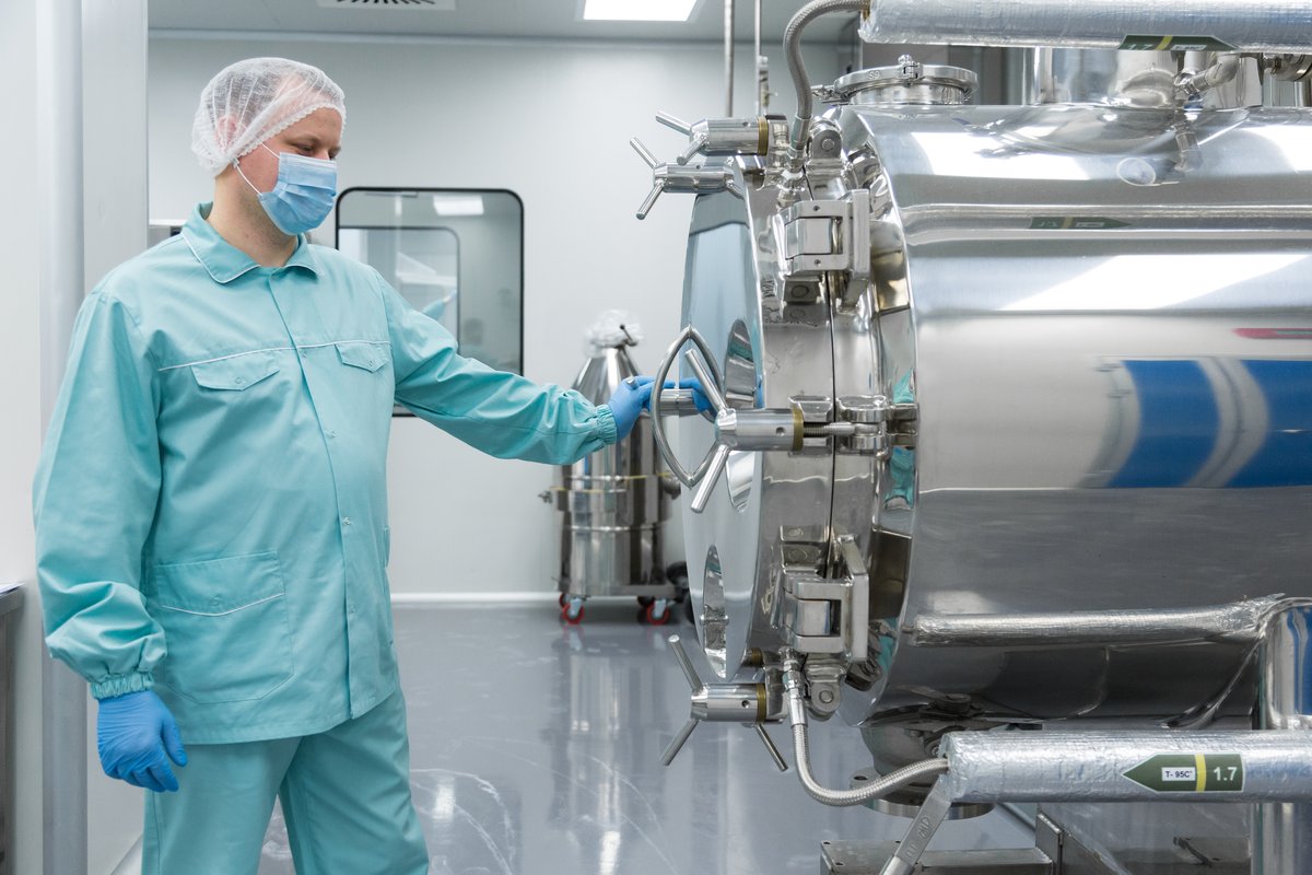 Illustrative photo: technician in protective clothing in front of a stainless steel tank